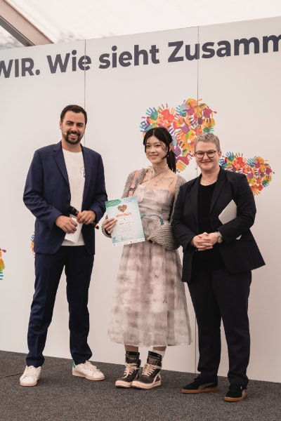 Stefanie (Mitte) aus Hannover bekommt in Luxemburg von Melanie Schmergal, Abteilungsleiterin Kommunikation und Öffentlichkeitsarbeit des Bundesverbandes der Deutschen Volksbanken und Raiffeisenbanken (BVR) und Vorsitzende der Internationalen Arbeitsgruppe „jugend creativ“ (rechts) sowie Moderator Raoul Roos (links) den traditionellen „jugend creativ“-Pokal und ihre Urkunde überreicht. Foto: Adrien Sensera, Banque Raiffeisen Société Coopérative